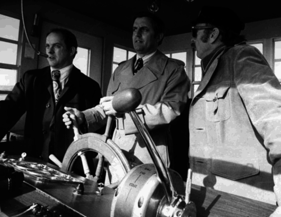 Senator Walter Mondale takes the helm of a paddlewheeler as Boundary Area Director James Harrison and Captain Bill Bowell look on
