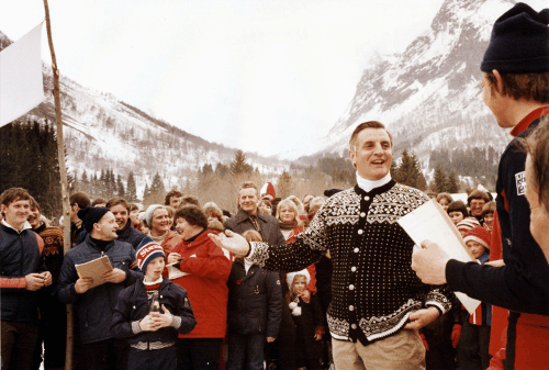 Walter Mondale in Norway, outdoors speaking to a crowd of people, with a mountain in the background.